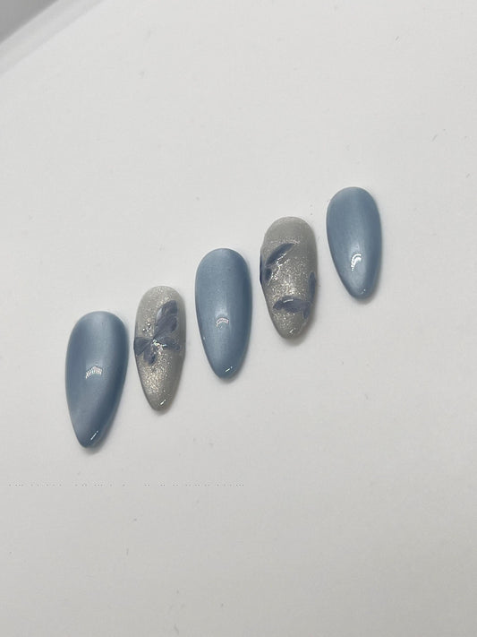 Handmade press-on nails with butterfly designs and cat-eye effect on a white background