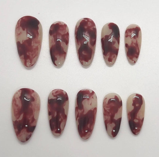 Handmade maroon and beige marbled press-on nails displayed on a white background