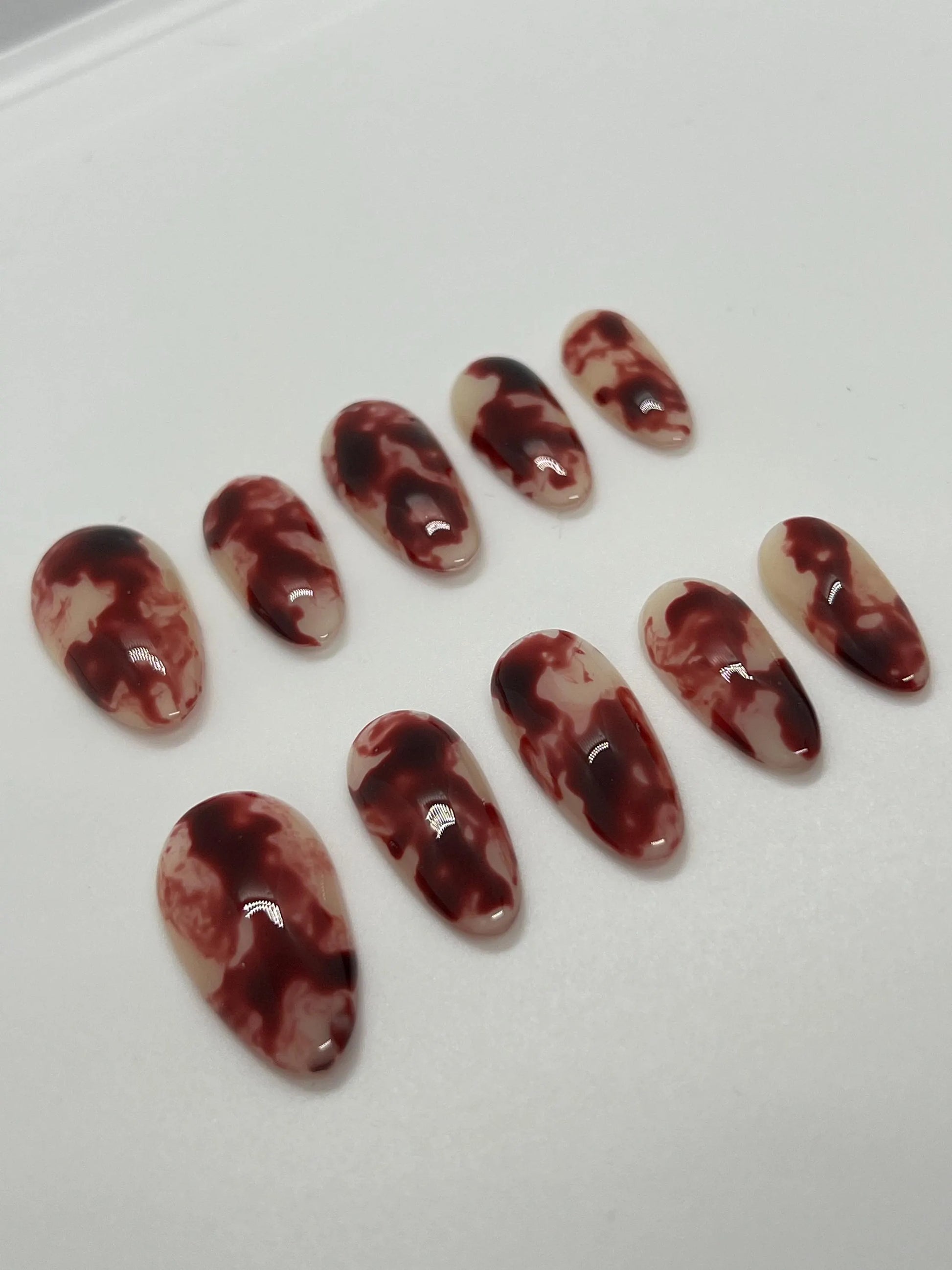Handmade maroon and beige marbled press-on nails displayed on a white background