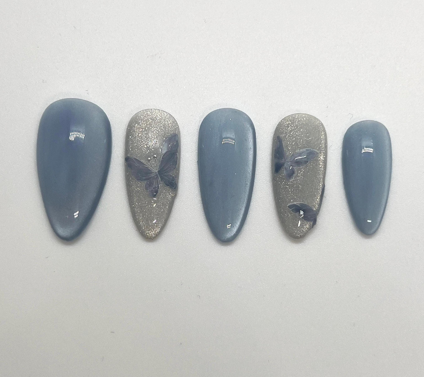 Handmade press-on nails with butterfly designs and cat-eye effect on a white background