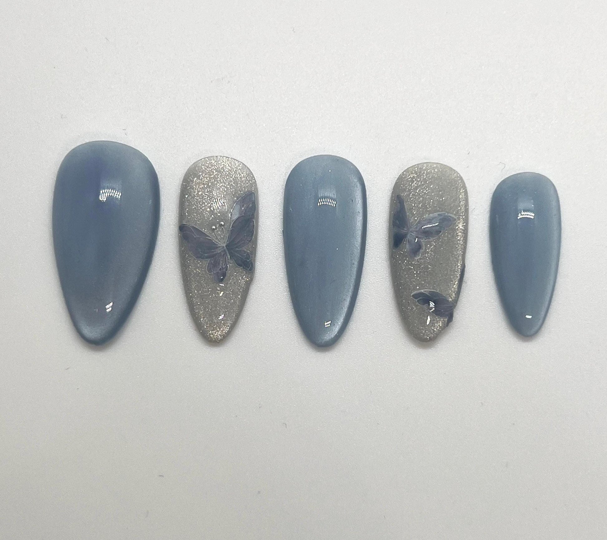 Handmade press-on nails with butterfly designs and cat-eye effect on a white background