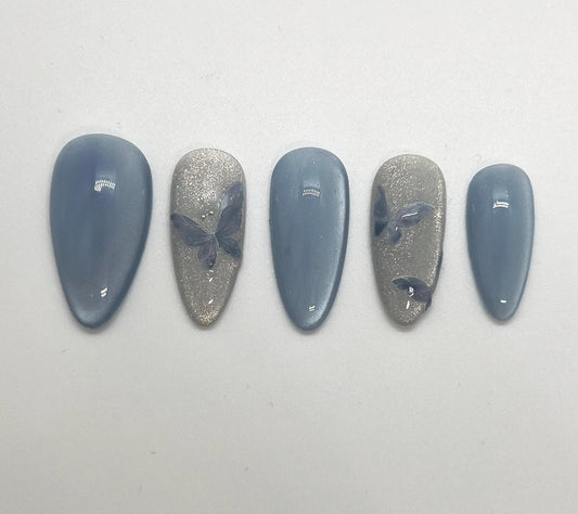 Handmade press-on nails with butterfly designs and cat-eye effect on a white background