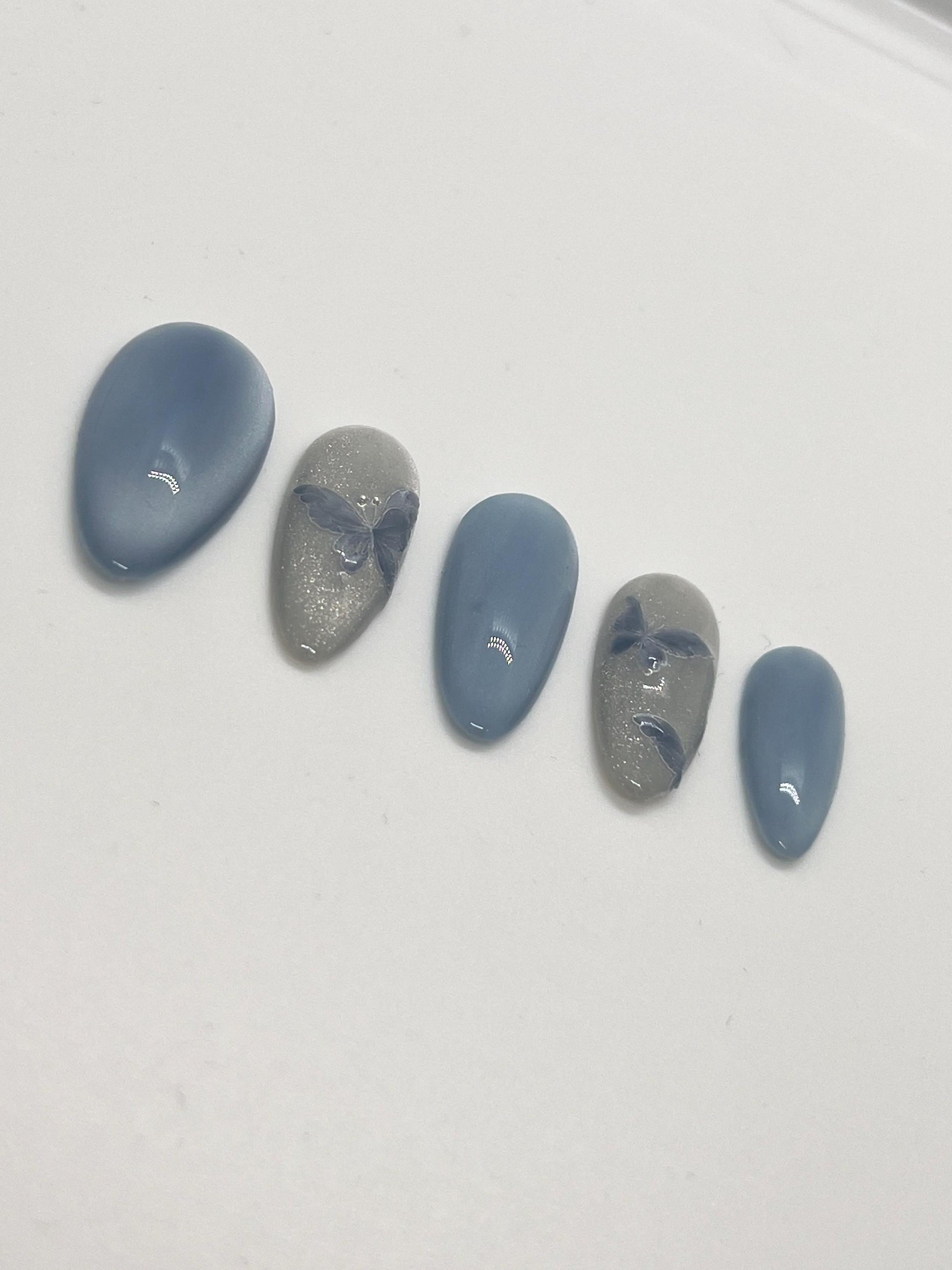 Handmade press-on nails with butterfly designs and cat-eye effect on a white background