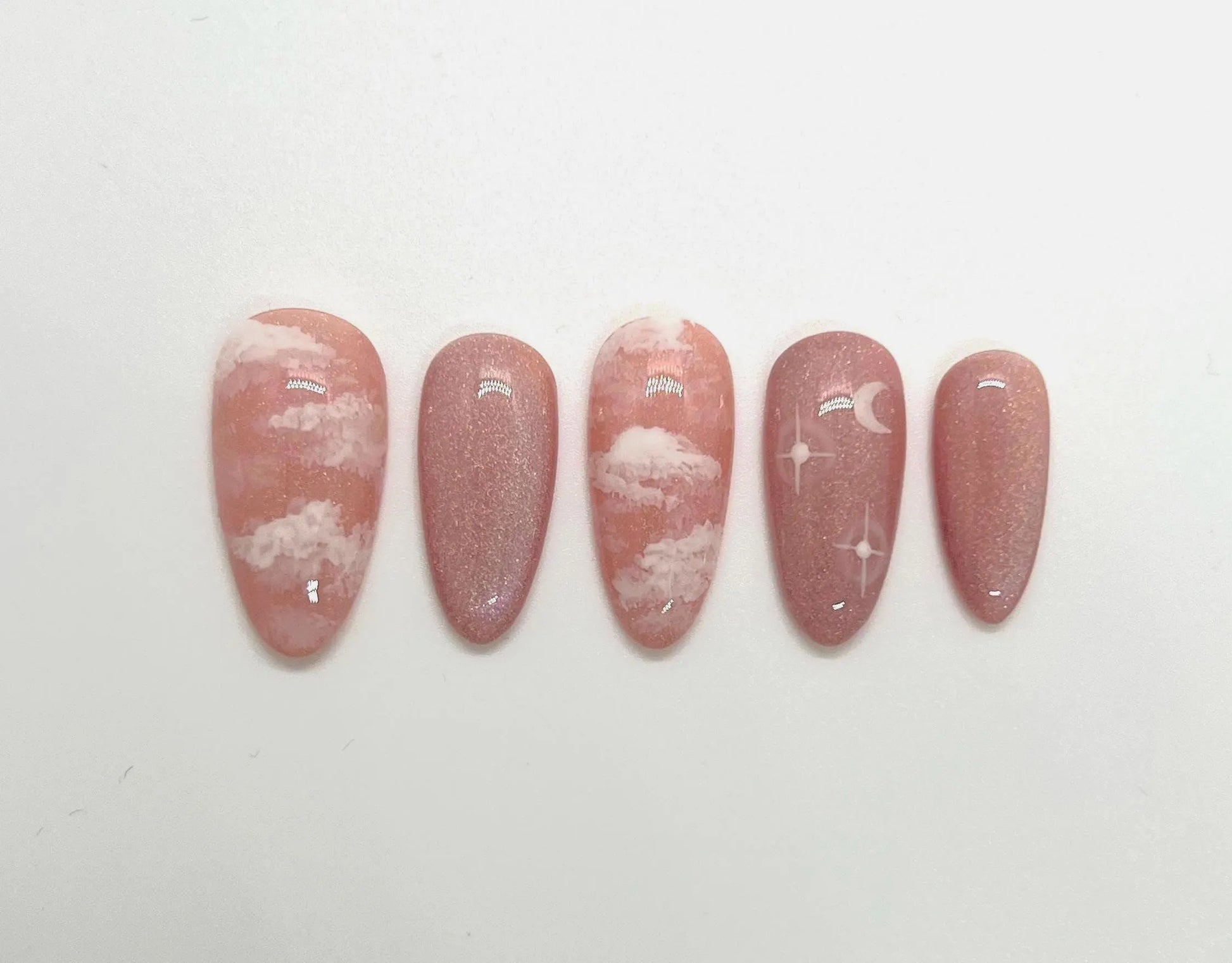 Handmade pink press-on nail samples with cloud and moon designs on a white background