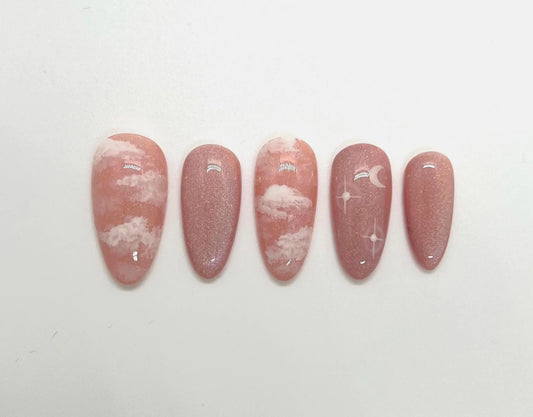 Handmade pink press-on nail samples with cloud and moon designs on a white background