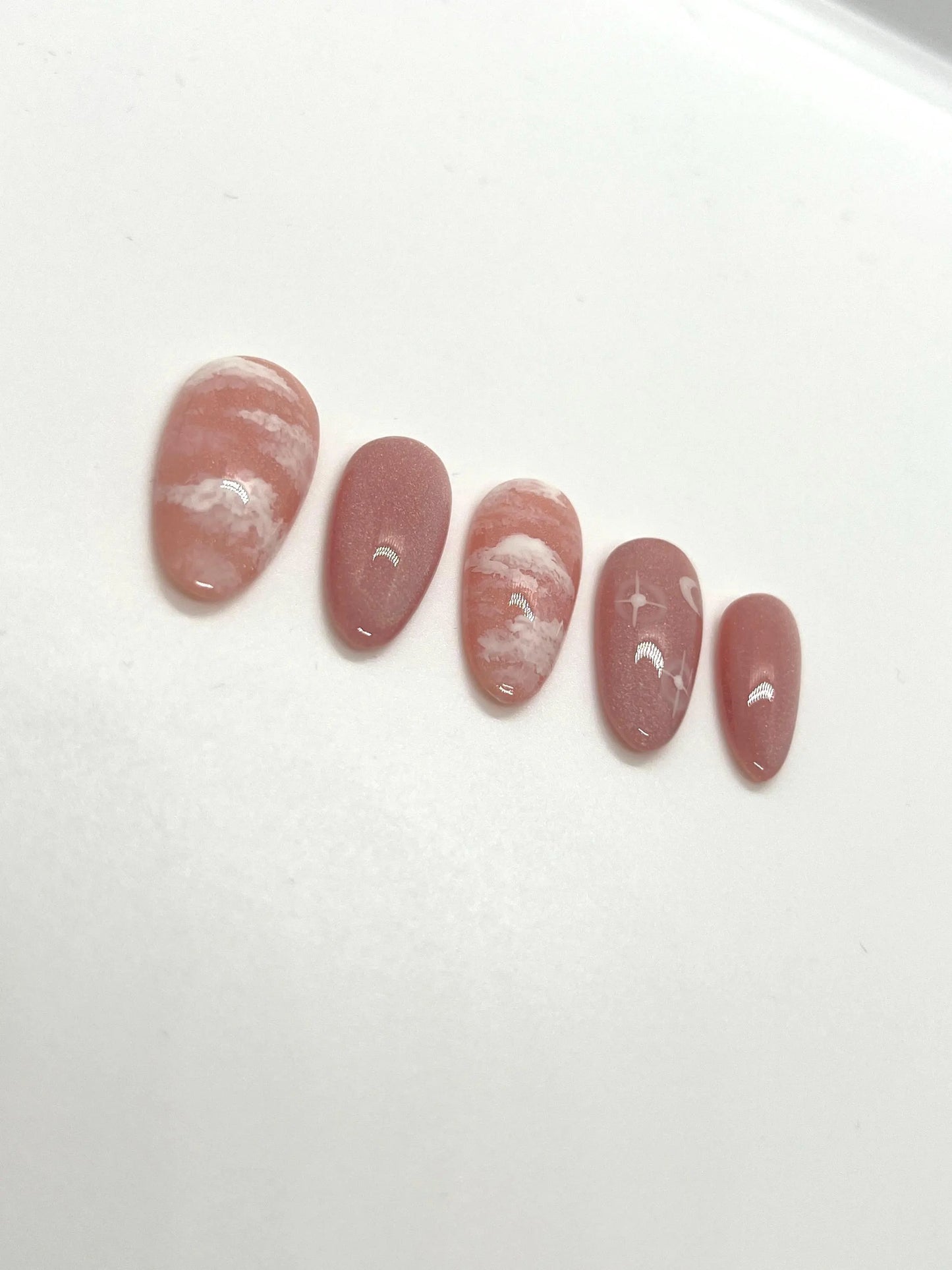Handmade pink press-on nail samples with cloud and moon designs on a white background