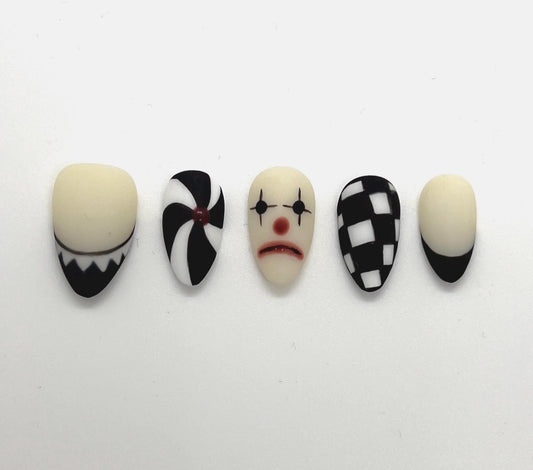 This striking black-and-white collection blends vintage circus vibes with gothic elegance, making it perfect for Halloween or any spooky-season look. Each nail features a unique design: twisted pinwheels, checkerboard patterns, and a sad clown face that adds the perfect amount of creepy charm.