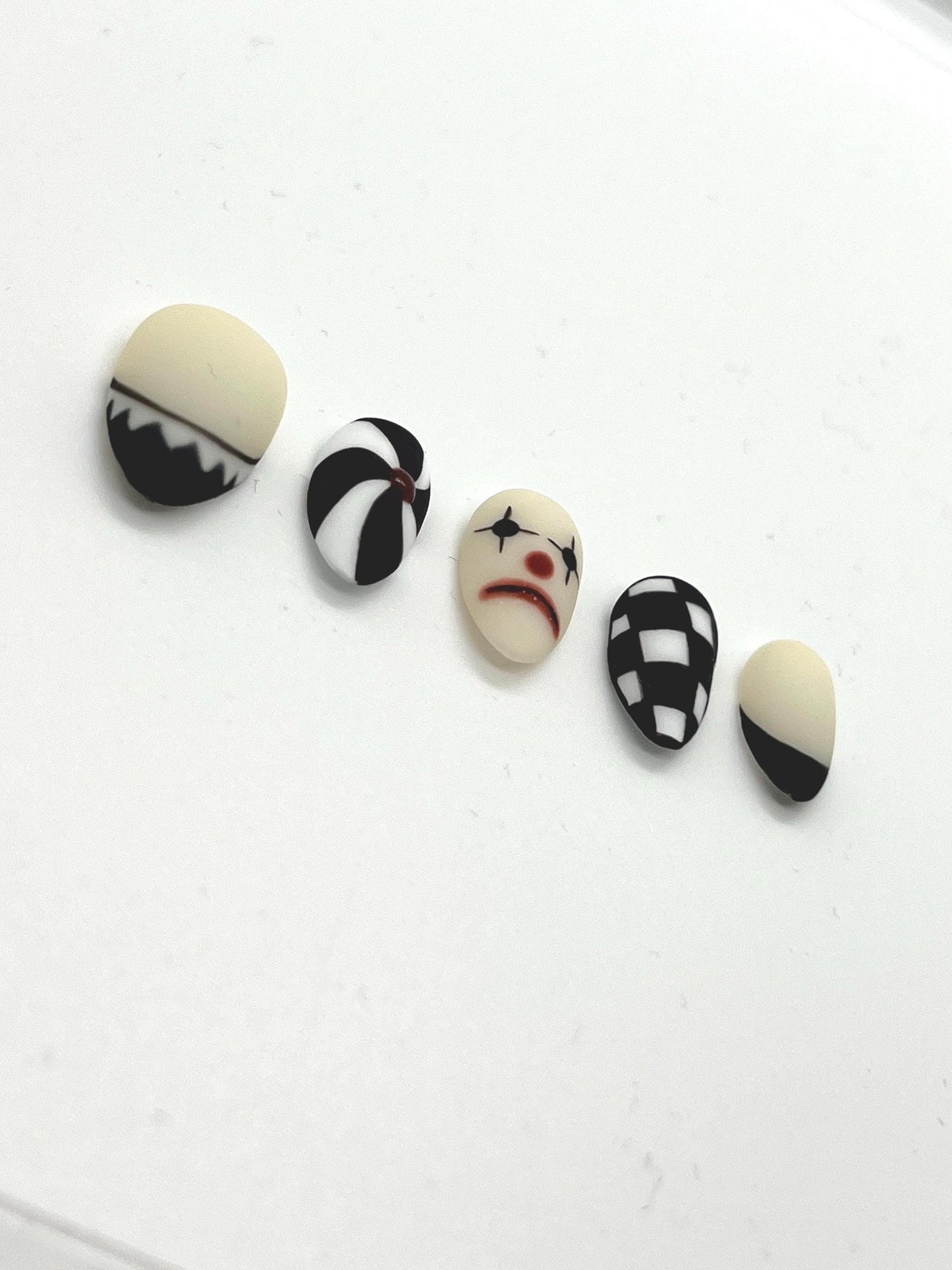 This striking black-and-white collection blends vintage circus vibes with gothic elegance, making it perfect for Halloween or any spooky-season look. Each nail features a unique design: twisted pinwheels, checkerboard patterns, and a sad clown face that adds the perfect amount of creepy charm.