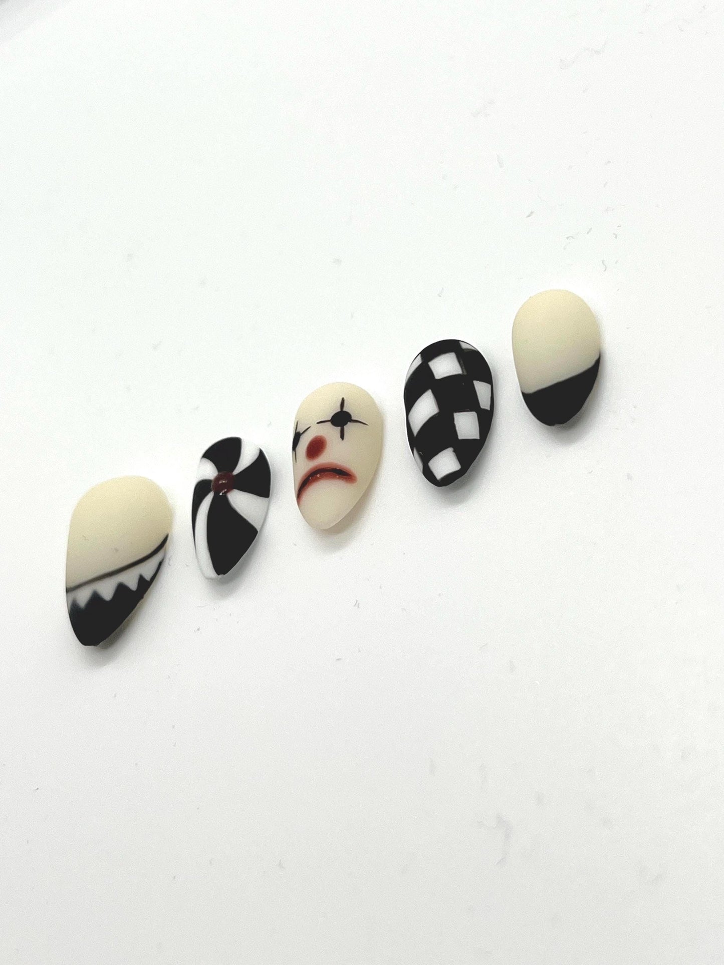 This striking black-and-white collection blends vintage circus vibes with gothic elegance, making it perfect for Halloween or any spooky-season look. Each nail features a unique design: twisted pinwheels, checkerboard patterns, and a sad clown face that adds the perfect amount of creepy charm.