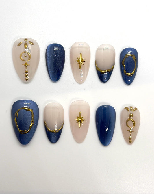Handmade press-on nails featuring blue, beige, and gold designs on a white background
