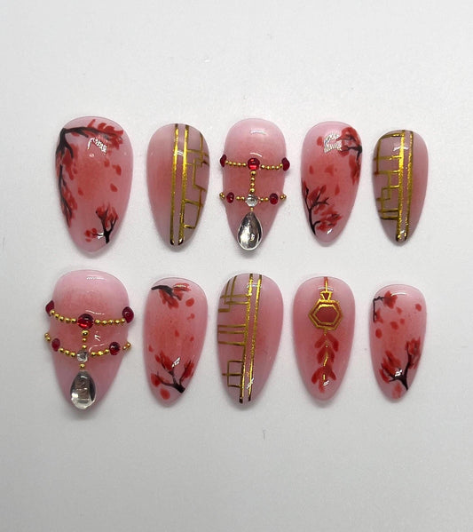 Handmade decorative press-on nails with pink base, gold patterns, and red accents on a white background