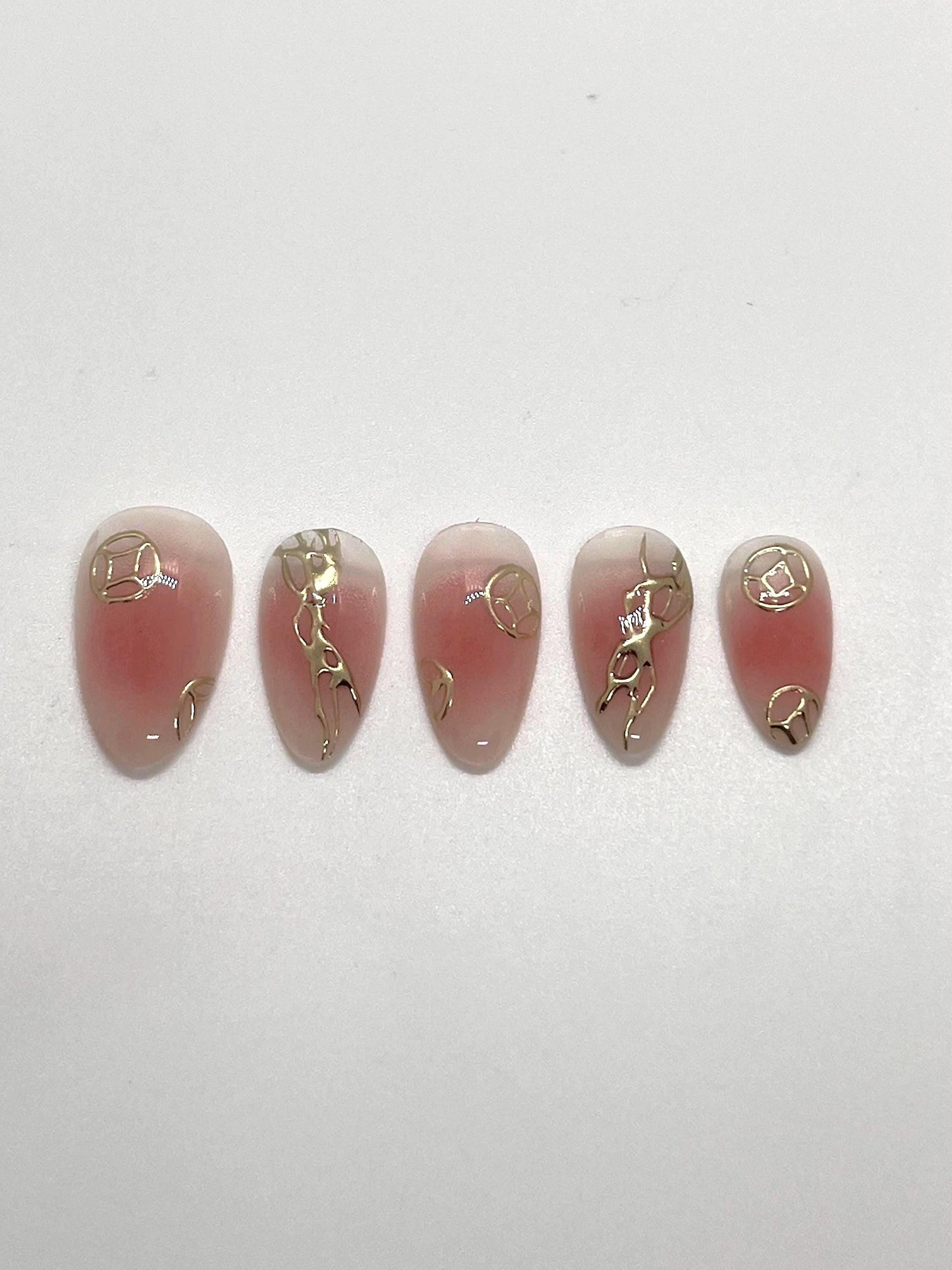 Handmade pink press-on nail samples with gold accents displayed on a white background