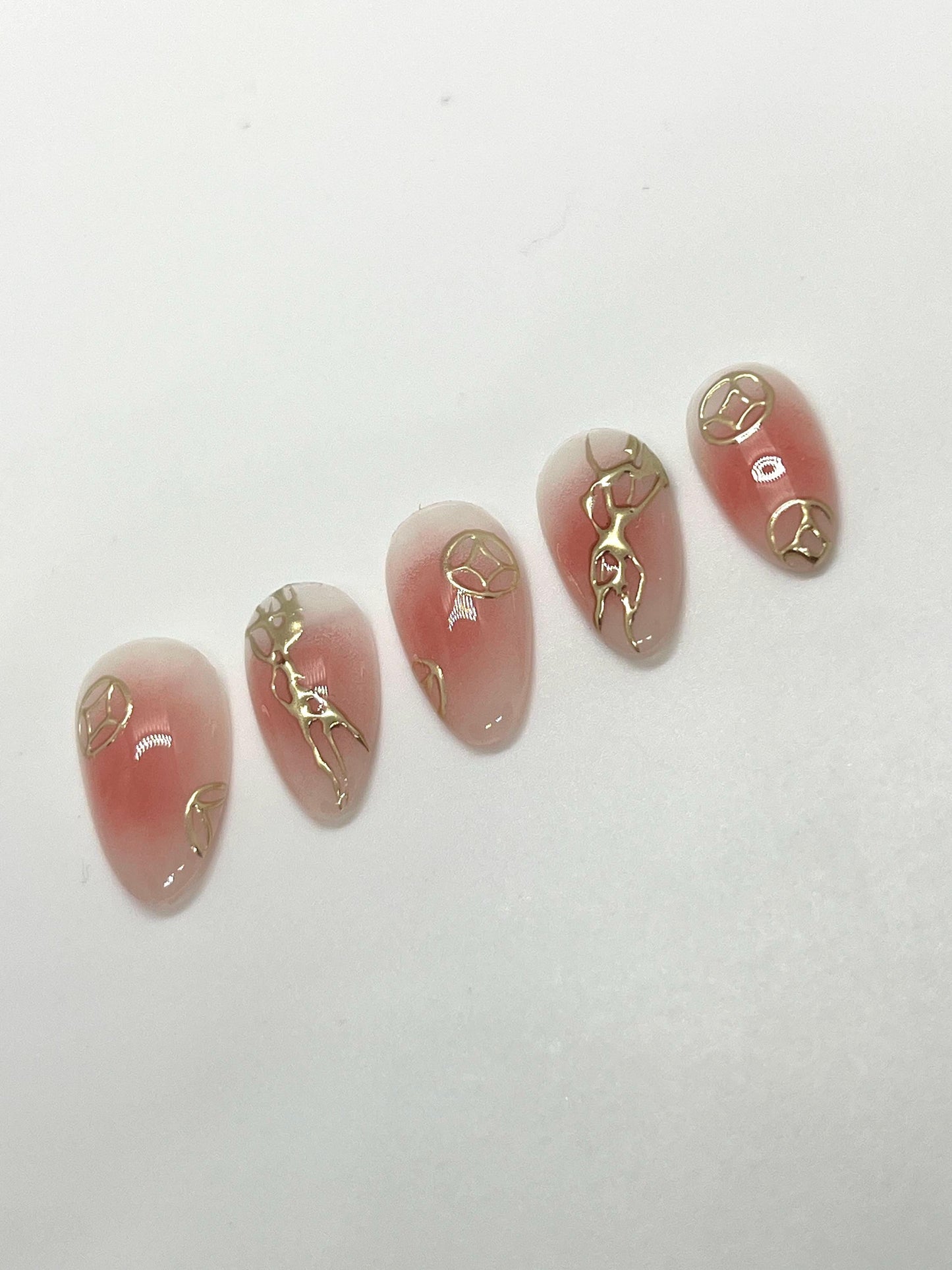 Handmade pink press-on nail samples with gold accents displayed on a white background
