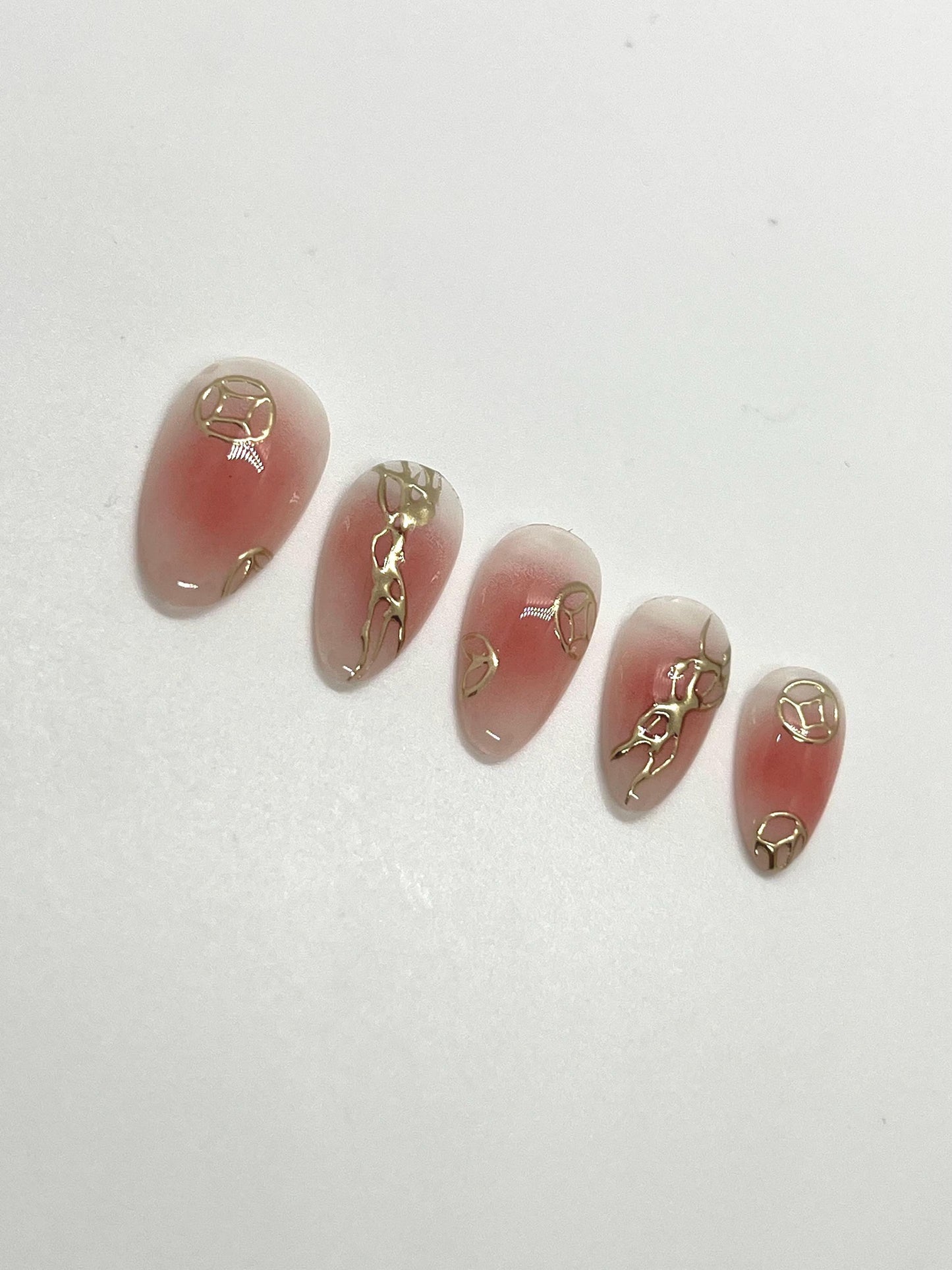 Handmade pink press-on nail samples with gold accents displayed on a white background
