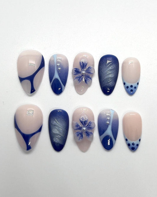 The Velvet Blueberry handmade press-on nail set features a soft nude base layered with rich, deep blueberry-blue tones. This elegant design blends velvety cat-eye shimmer with abstract swirls, delicate floral accents, and subtle dot details for a refined yet cozy aesthetic.