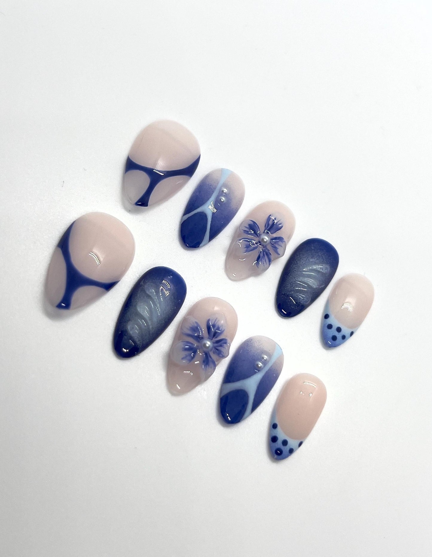 The Velvet Blueberry handmade press-on nail set features a soft nude base layered with rich, deep blueberry-blue tones. This elegant design blends velvety cat-eye shimmer with abstract swirls, delicate floral accents, and subtle dot details for a refined yet cozy aesthetic.