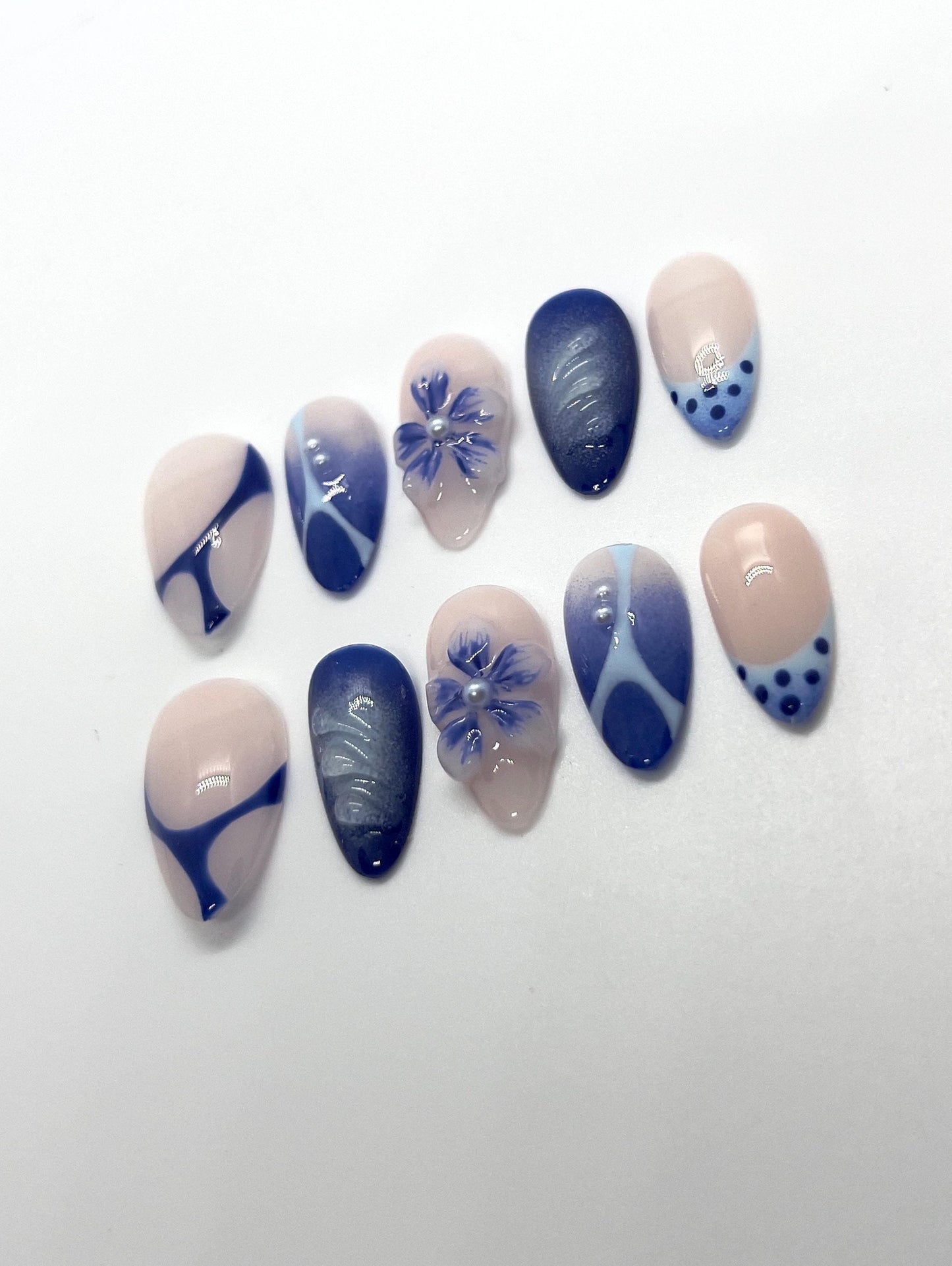The Velvet Blueberry handmade press-on nail set features a soft nude base layered with rich, deep blueberry-blue tones. This elegant design blends velvety cat-eye shimmer with abstract swirls, delicate floral accents, and subtle dot details for a refined yet cozy aesthetic.